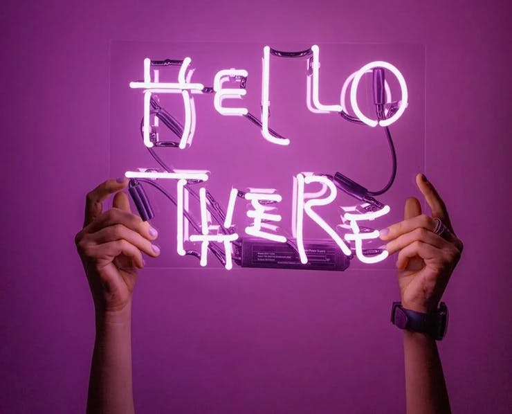 Two hands hold a neon light sign with the words "Hello there"