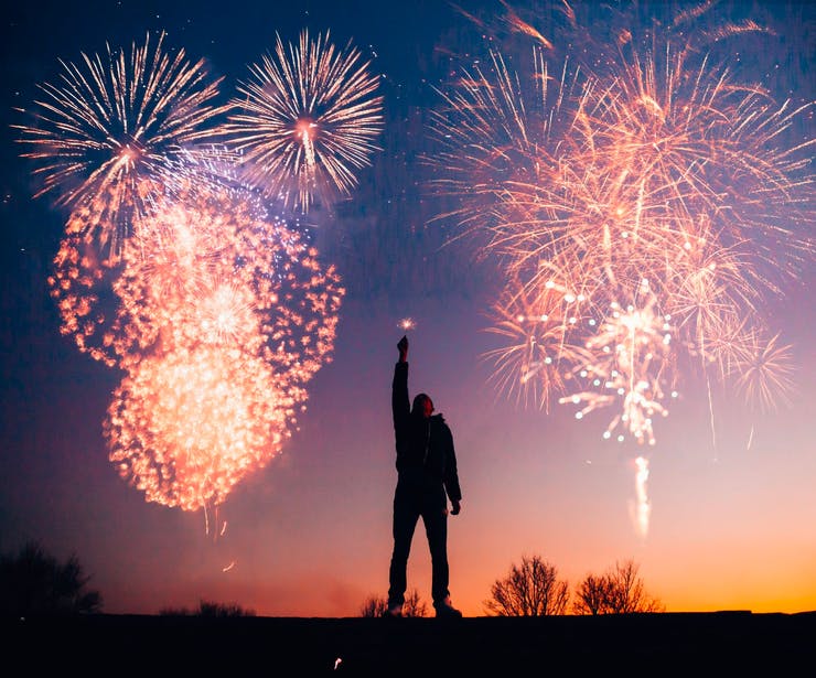 Silhouette of a man in front of a night sky illuminated by fireworks